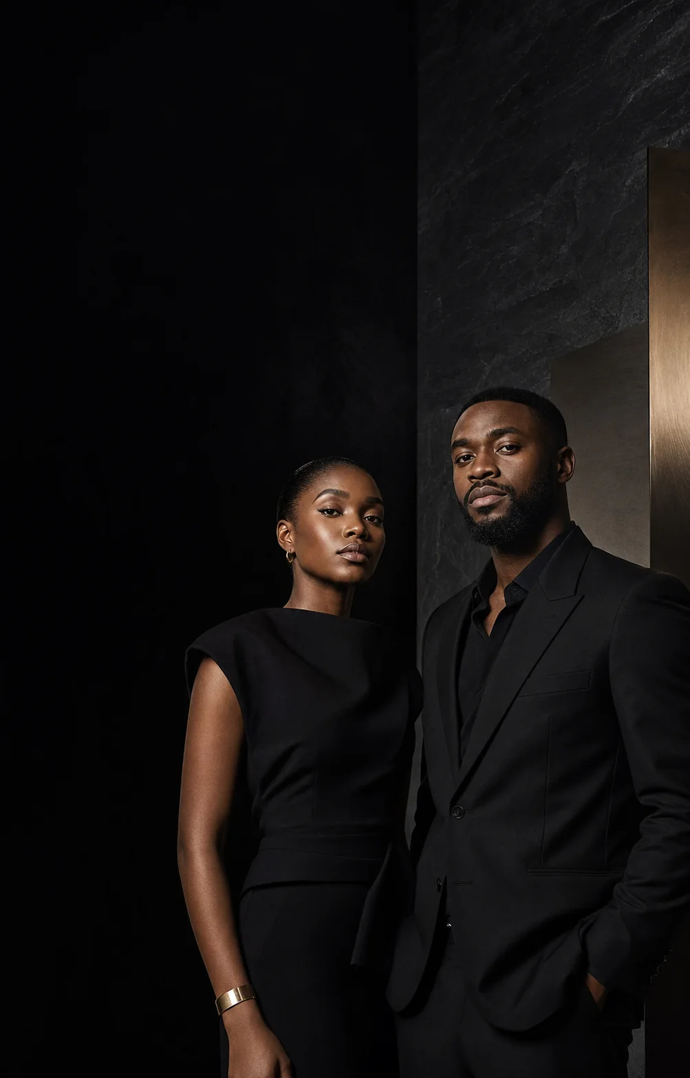 Two members in black against a dark stone wall with gold light